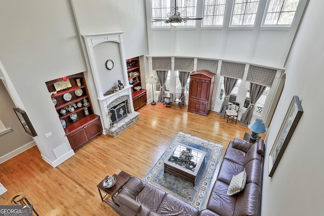 living area with baseboards, ceiling fan, light wood-style flooring, a fireplace, and a towering ceiling