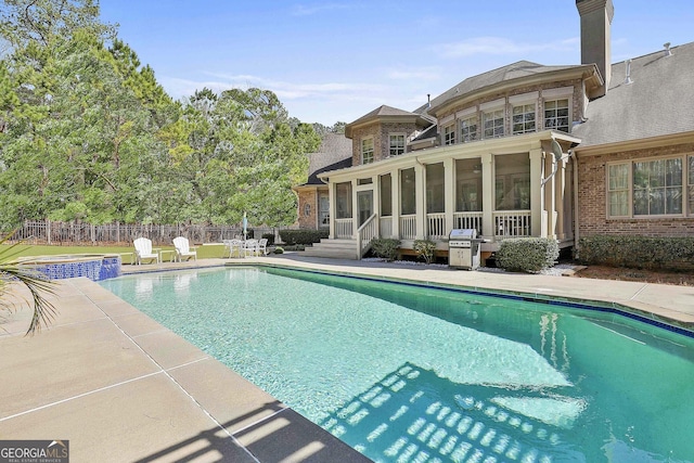 view of swimming pool featuring a pool with connected hot tub, a patio, fence, a grill, and a sunroom