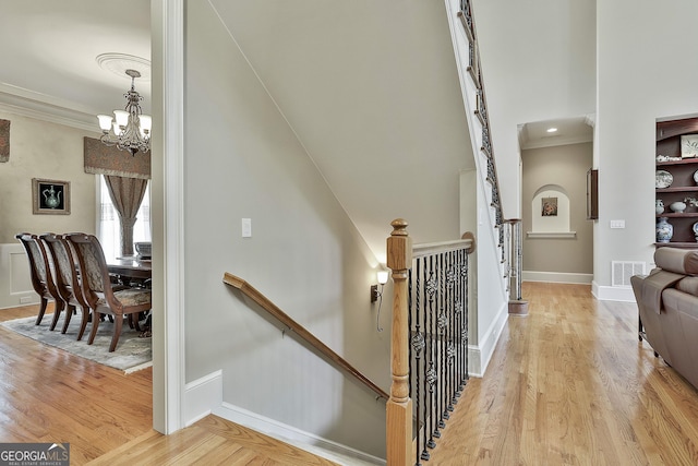 stairs with an inviting chandelier, crown molding, wood finished floors, and visible vents