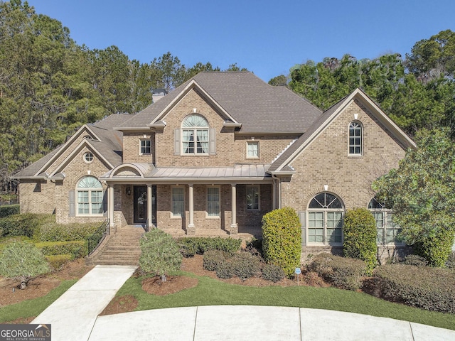 traditional-style home with brick siding, covered porch, a chimney, and a shingled roof