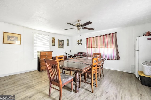 dining room with baseboards, light wood-style floors, a ceiling fan, and a textured ceiling