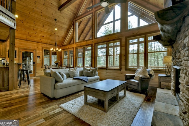 living room with ceiling fan with notable chandelier, wood finished floors, wooden walls, a fireplace, and wood ceiling