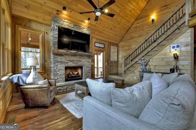 living area with wood finished floors, wooden walls, a fireplace, wood ceiling, and stairs