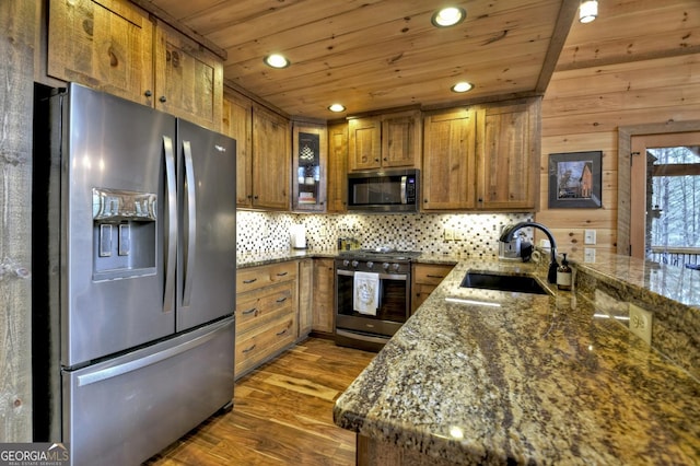 kitchen with a sink, backsplash, appliances with stainless steel finishes, brown cabinetry, and wood ceiling