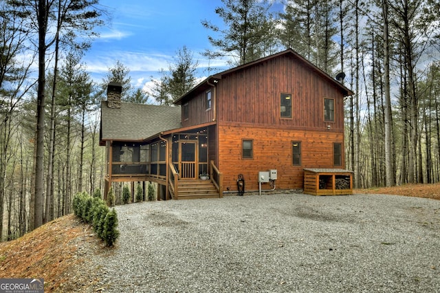 rear view of house featuring a chimney, gravel driveway, roof with shingles, and a sunroom