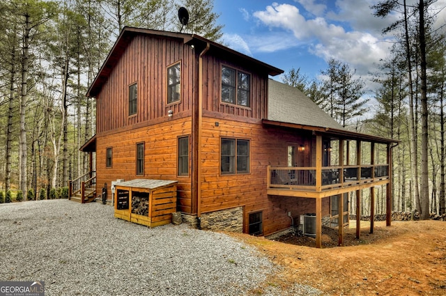 rear view of property featuring a deck, cooling unit, board and batten siding, and roof with shingles