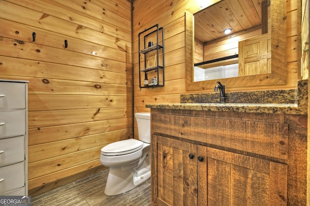 bathroom featuring vanity, toilet, wood finished floors, and wooden walls