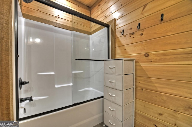 bathroom featuring wood walls and shower / bath combination with glass door