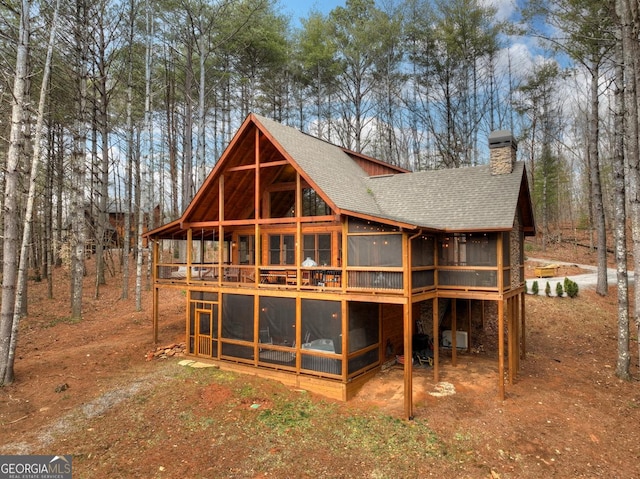 back of property with a chimney, a shingled roof, and a sunroom