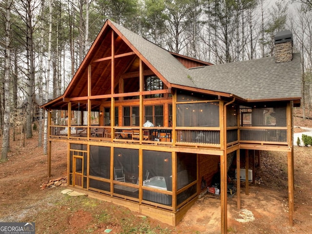 rear view of property with roof with shingles, a chimney, and a sunroom