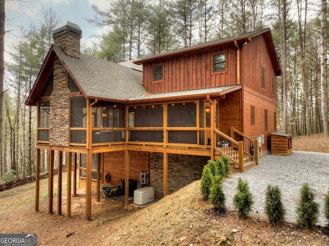 back of property with stone siding, roof with shingles, a chimney, and a sunroom