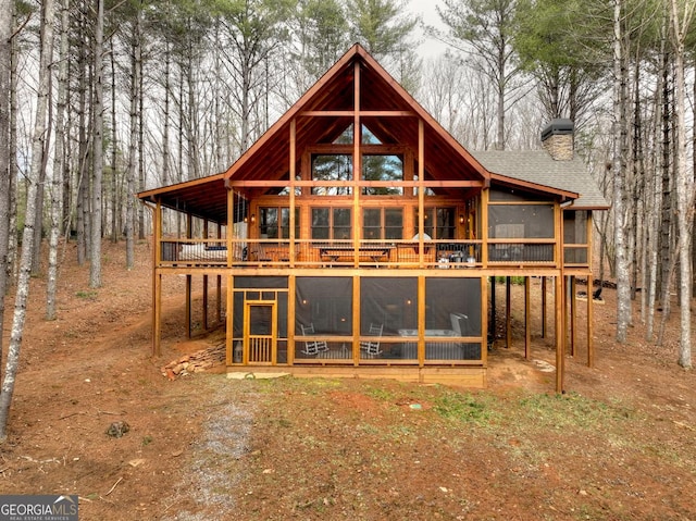 rear view of house featuring roof with shingles, a sunroom, and a chimney