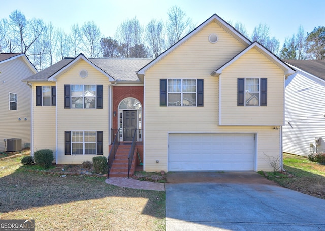 split foyer home featuring a garage, central AC unit, driveway, and a shingled roof