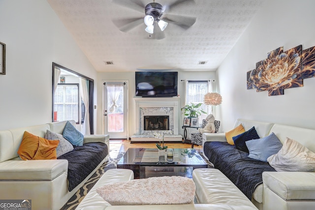 living area featuring visible vents, a textured ceiling, a premium fireplace, and vaulted ceiling