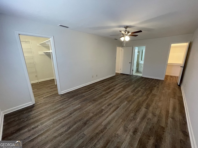 unfurnished bedroom featuring a spacious closet, dark wood-style floors, visible vents, and a closet