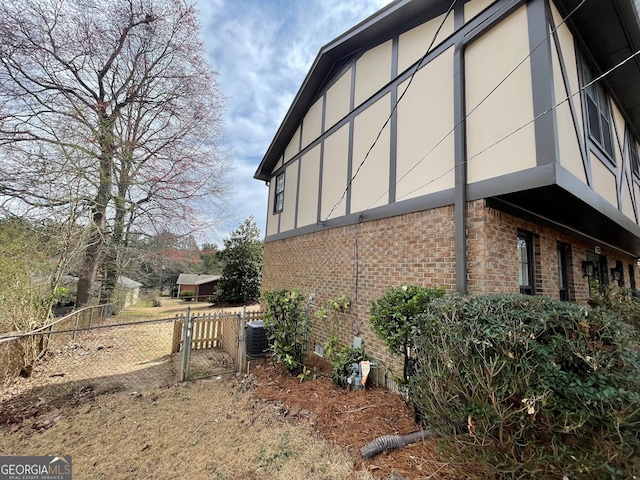 view of property exterior with stucco siding, a gate, fence, brick siding, and central AC unit