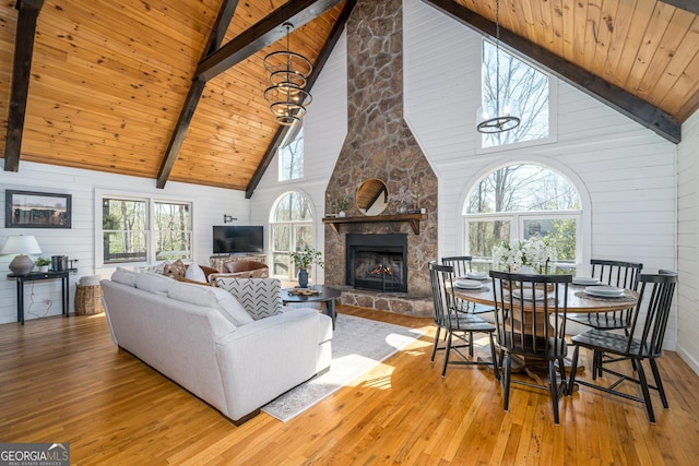 living room with a stone fireplace, beamed ceiling, wood ceiling, and hardwood / wood-style floors