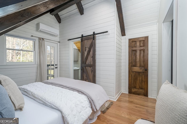 bedroom with wooden walls, lofted ceiling with beams, a barn door, a wall unit AC, and light wood-style floors