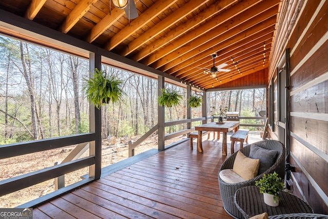 sunroom featuring wood ceiling, vaulted ceiling with beams, a ceiling fan, and a wooded view