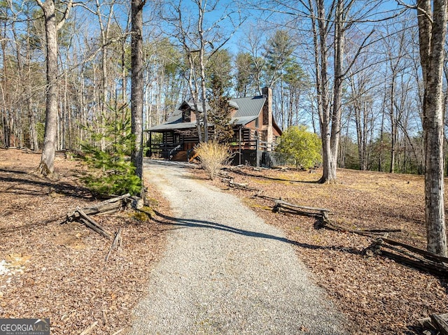 view of front of property with log siding, a chimney, gravel driveway, and metal roof