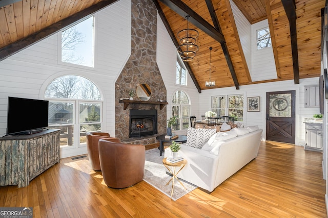 living area with light wood finished floors, beam ceiling, a fireplace, a skylight, and wooden ceiling