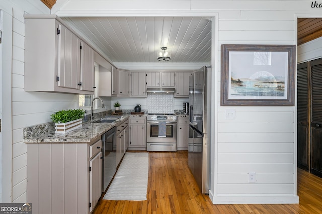 kitchen featuring light stone counters, light wood-style floors, appliances with stainless steel finishes, and a sink