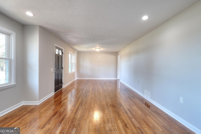 unfurnished room with visible vents, a healthy amount of sunlight, a textured ceiling, and wood finished floors