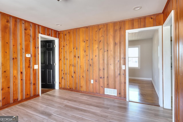 empty room with visible vents, baseboards, wood walls, and light wood finished floors