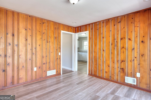 spare room featuring wooden walls, wood finished floors, and visible vents