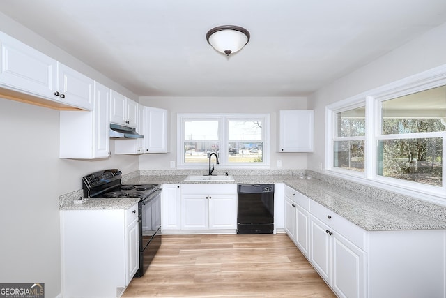 kitchen featuring under cabinet range hood, light stone counters, white cabinets, black appliances, and a sink