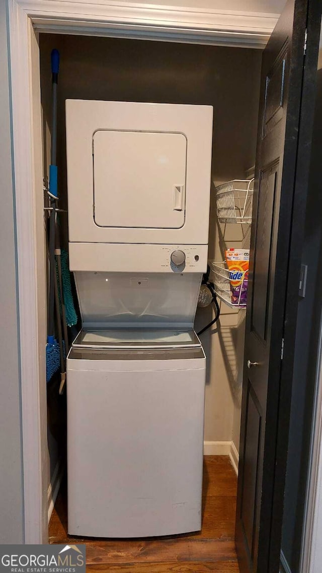 clothes washing area with laundry area, baseboards, stacked washer / drying machine, and dark wood-style flooring