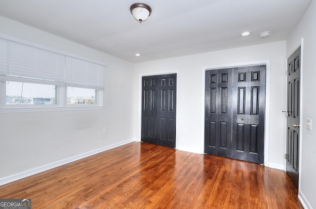 unfurnished bedroom featuring recessed lighting, wood finished floors, multiple closets, and baseboards