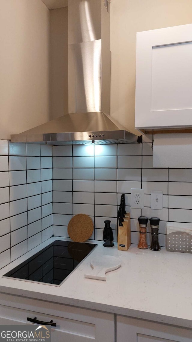 kitchen featuring backsplash, wall chimney range hood, light stone countertops, white cabinetry, and black electric cooktop