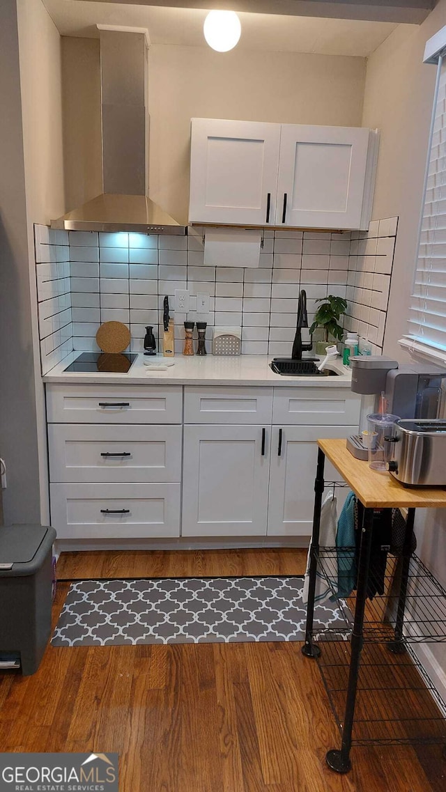 kitchen featuring a sink, light countertops, wall chimney exhaust hood, and wood finished floors