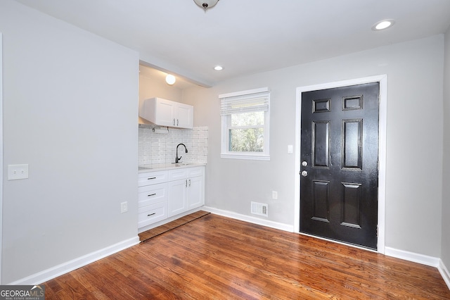 interior space featuring visible vents, dark wood-type flooring, decorative backsplash, white cabinetry, and a sink