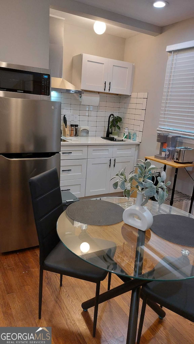 kitchen featuring a sink, tasteful backsplash, wood finished floors, appliances with stainless steel finishes, and wall chimney exhaust hood