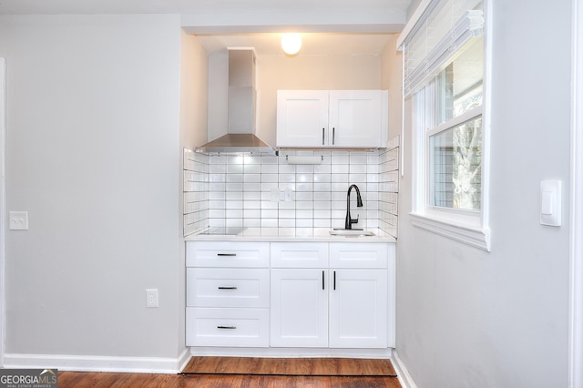 kitchen with tasteful backsplash, white cabinetry, wall chimney range hood, and a sink