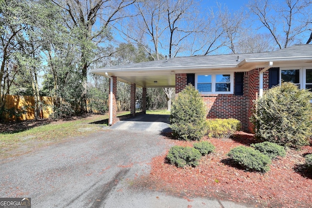 exterior space with brick siding, an attached carport, driveway, and fence