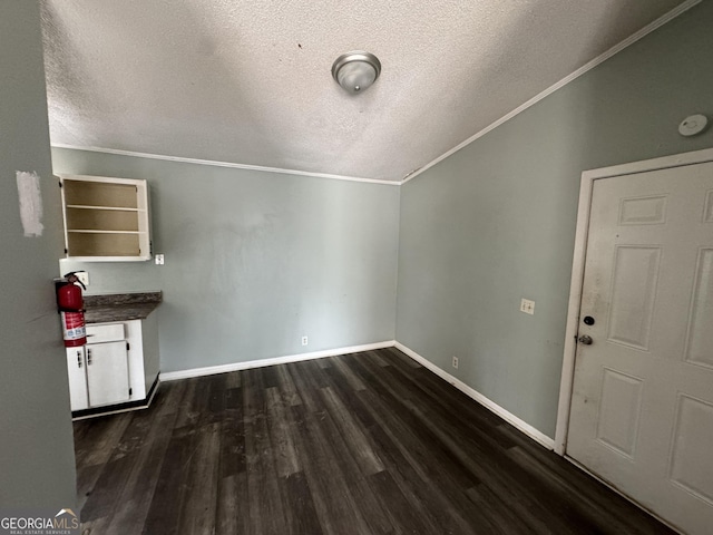 unfurnished dining area with baseboards, dark wood finished floors, lofted ceiling, ornamental molding, and a textured ceiling