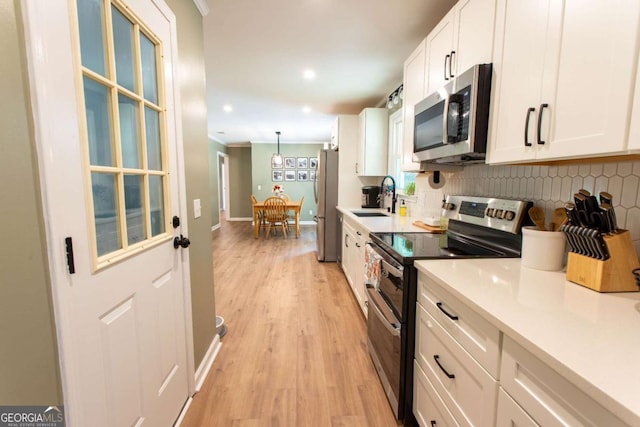 kitchen featuring ornamental molding, decorative backsplash, a sink, appliances with stainless steel finishes, and white cabinetry