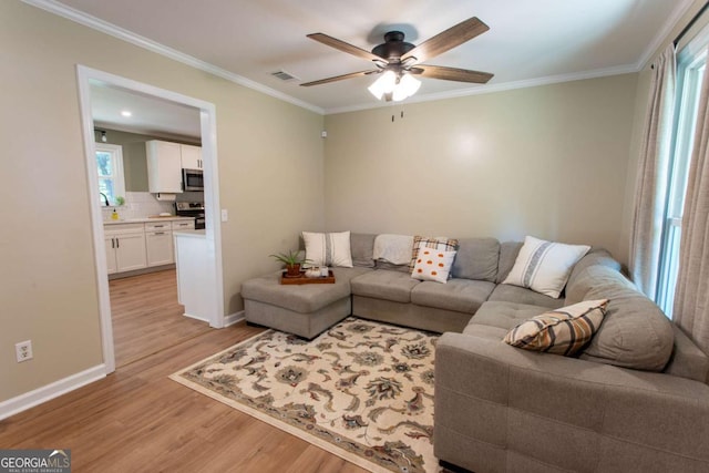 living area featuring visible vents, crown molding, baseboards, light wood-type flooring, and a ceiling fan