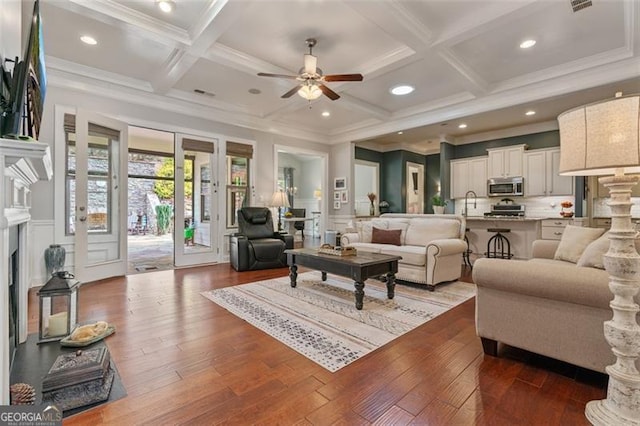 living room featuring beam ceiling, dark wood-style floors, coffered ceiling, and a wainscoted wall