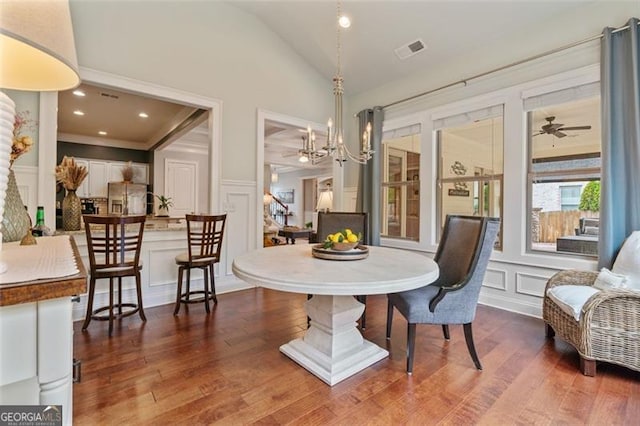 dining room with visible vents, ceiling fan with notable chandelier, wood finished floors, a decorative wall, and lofted ceiling