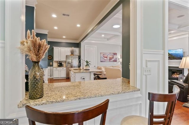 kitchen with visible vents, ornamental molding, beam ceiling, white cabinets, and stainless steel fridge