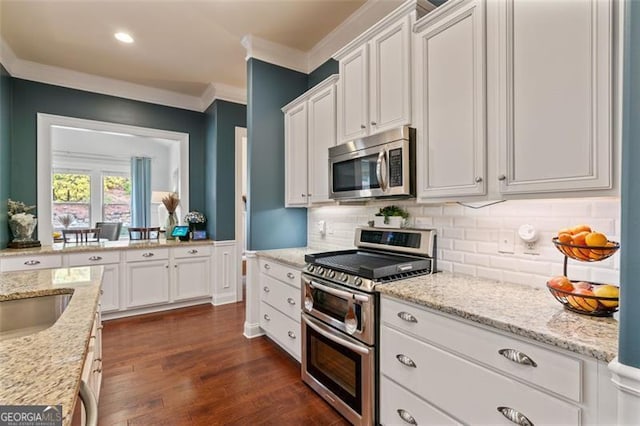 kitchen with light stone counters, dark wood finished floors, ornamental molding, white cabinets, and appliances with stainless steel finishes