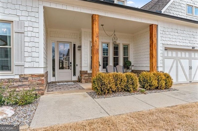 doorway to property with a garage, stone siding, and covered porch