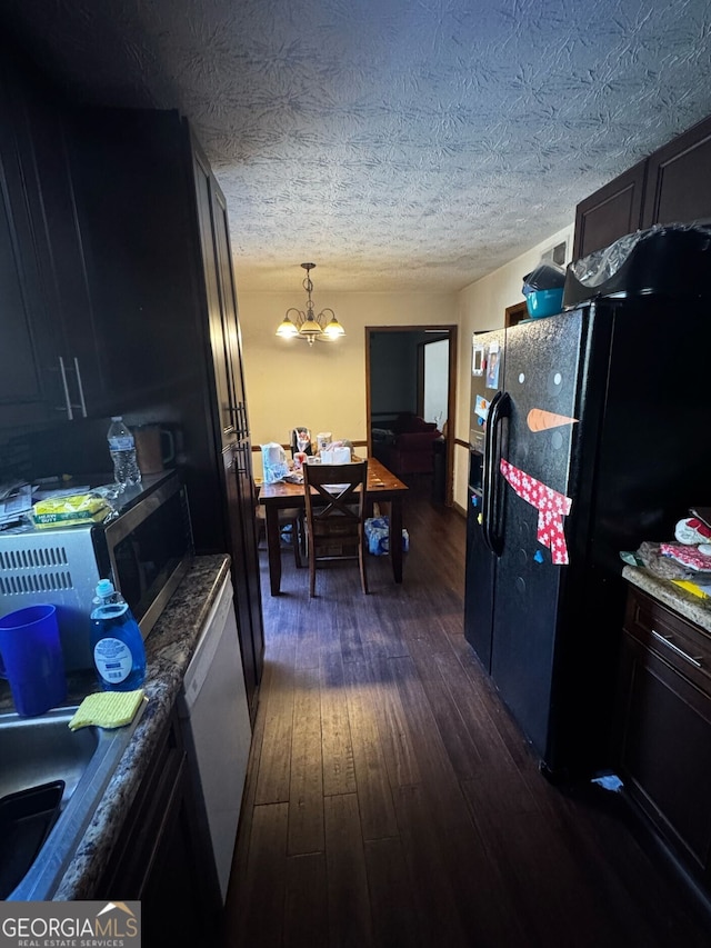 kitchen featuring a notable chandelier, black fridge, stainless steel microwave, a textured ceiling, and dark wood-style flooring