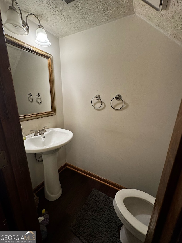 half bath featuring toilet, a sink, a textured ceiling, wood finished floors, and baseboards