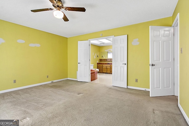 unfurnished bedroom featuring ensuite bathroom, a ceiling fan, a textured ceiling, carpet flooring, and baseboards