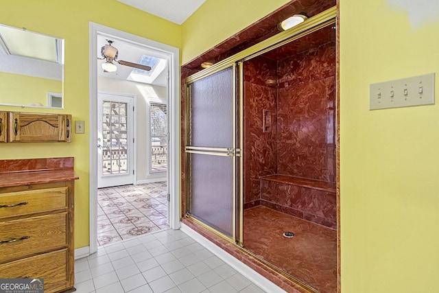 full bath with ceiling fan, a skylight, a shower stall, and tile patterned flooring